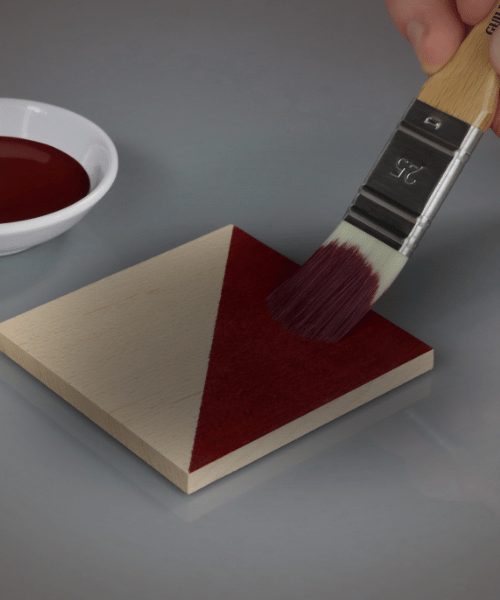 Person painting a triangle on a wooden block with a brush and red paint.