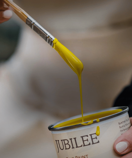 Yellow paint being dripped from a brush into a can labeled 'Jubilee'.