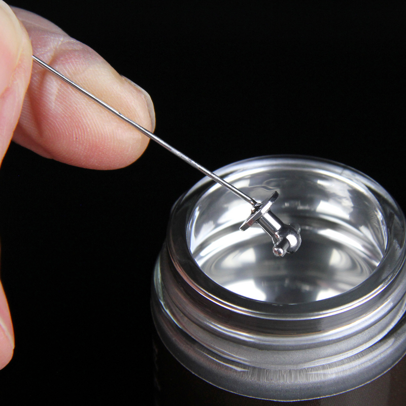 Metallic container with a lid being opened by a hand holding a small tool against a black background