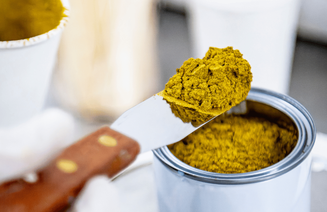 Gold metallic pigment container with a scoop of pigment on an art spatula