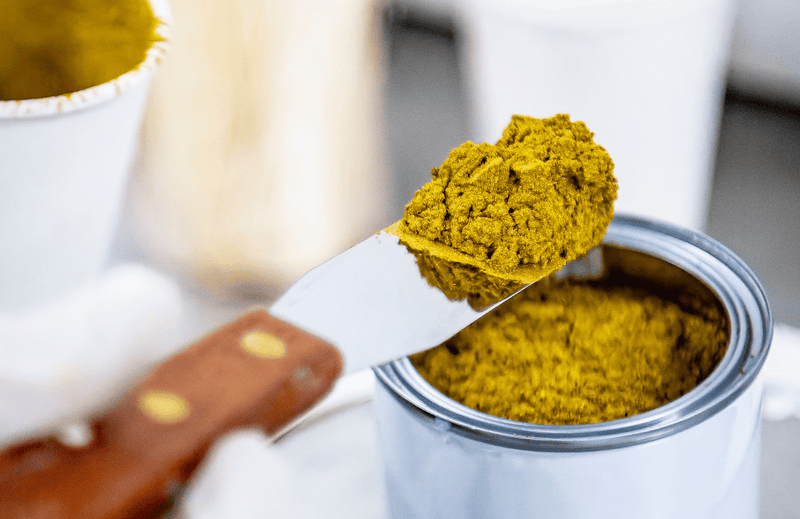 Gold metallic pigment container with a scoop of pigment on an art spatula