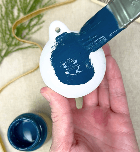 Hand painting a blue design on a white ornament with a brush.