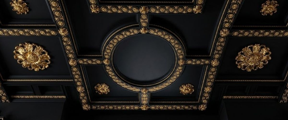 An ornate black ceiling with elaborate gold decorative molding, rosettes, and a central oval medallion.