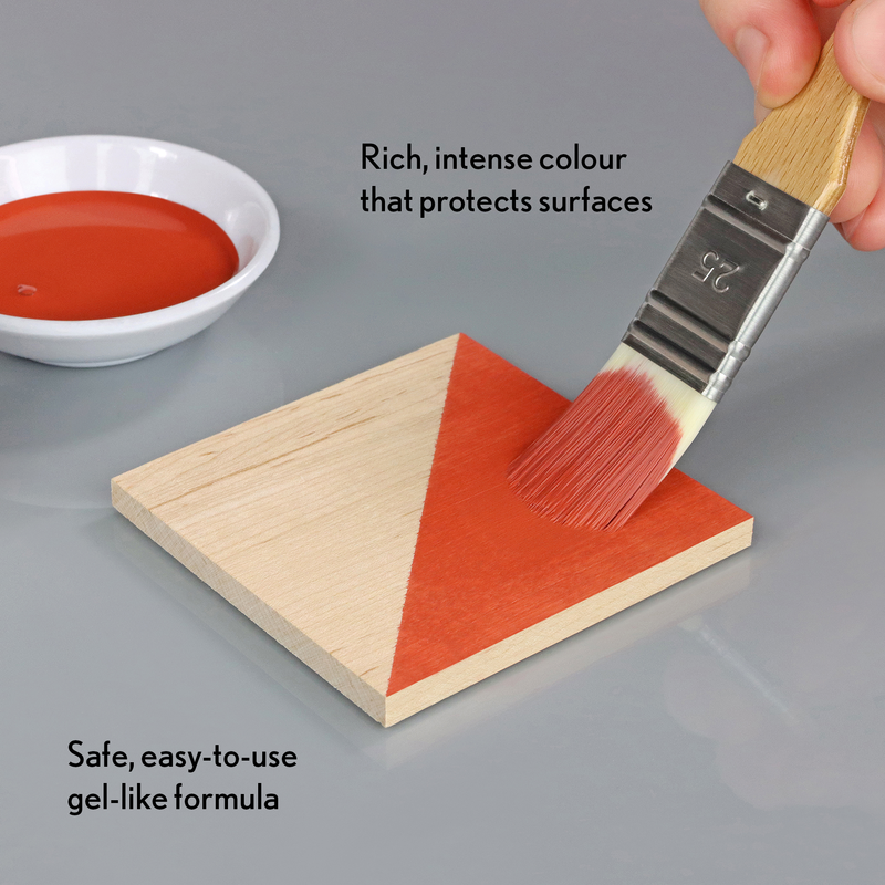 Person applying red paint to a wooden triangle with a brush, next to a bowl of paint.
