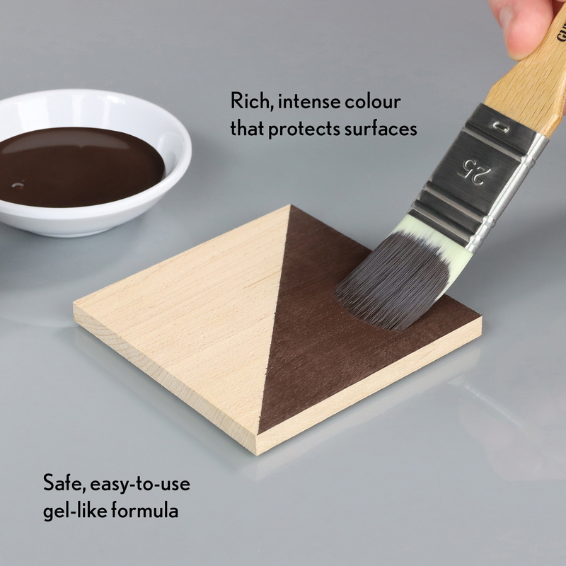 Wooden triangle being painted with a brush into a dark brown colour, next to a bowl of dark brown liquid and a brush.