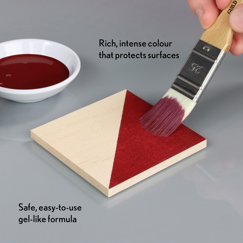 Person applying red paint to a wooden triangle with a brush, next to a bowl of paint.
