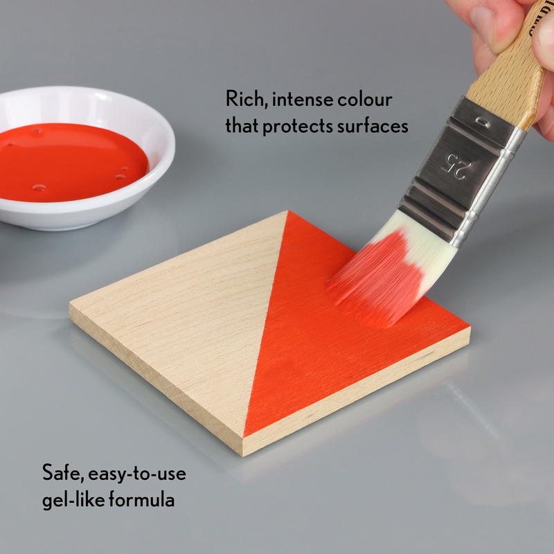 Person applying red paint to a wooden triangle with a brush, next to a bowl of paint.