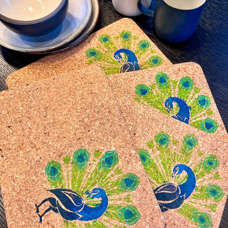 Cork coasters with peacock design on a table with cups and saucers.