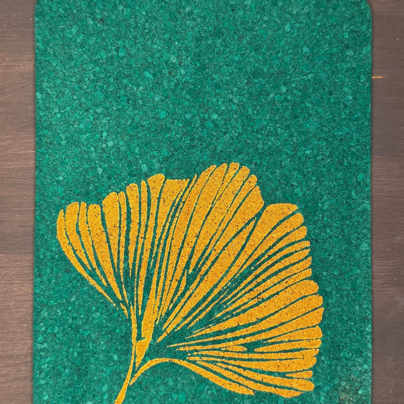 Green textured cork mat with a gold leaf design on a wooden surface