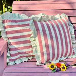 
                      
                        Pink and white striped pillows with ruffles on a pink wooden bench with flowers.
                      
                    