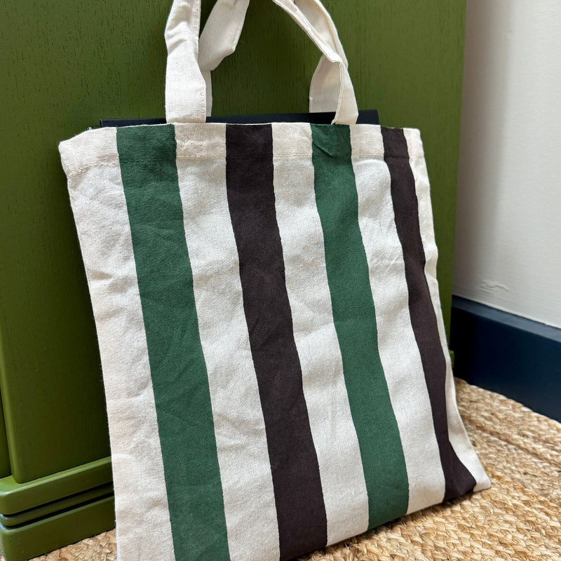Striped tote bag with green and brown stripes on a woven surface against a green wall.