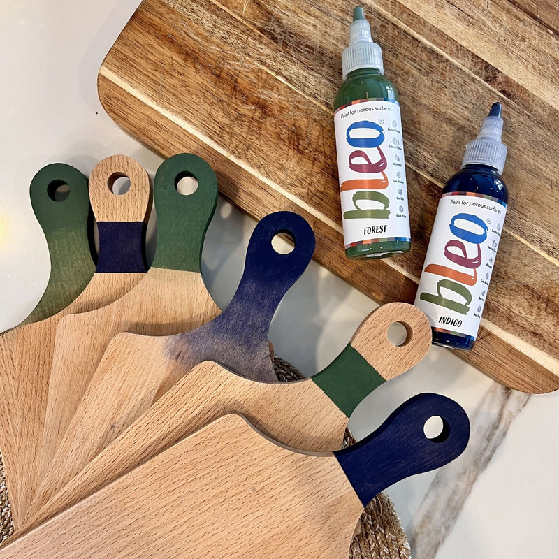 Wooden boards with colourful handles on a wooden surface, accompanied by bottles labelled 'Bleo'.