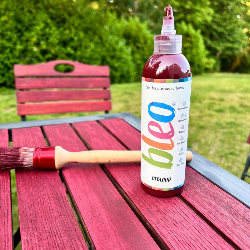 Bottle of Oxblood paint with a brush on a red wooden surface outdoors