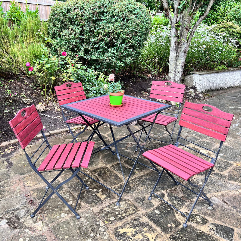 Red outdoor table and chairs set on a stone patio with garden background