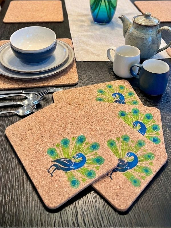 Cork coasters with peacock design on a table setting with cups, bowls, and a teapot.