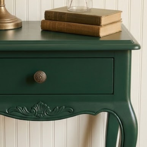 
                      
                        Close up of a dark green painted side table in front of a board and batten wall
                      
                    