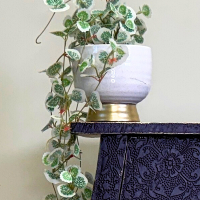 White pot with green leaves on a decorative purple stand against a plain background