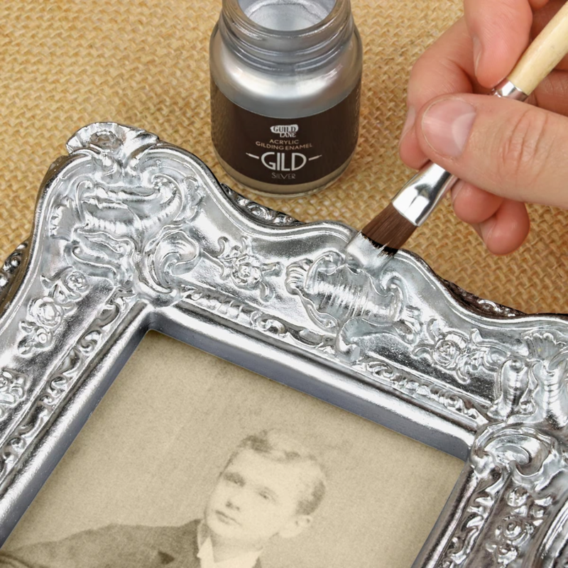 Person gilding an ornate silver frame with a brush and gold paint.