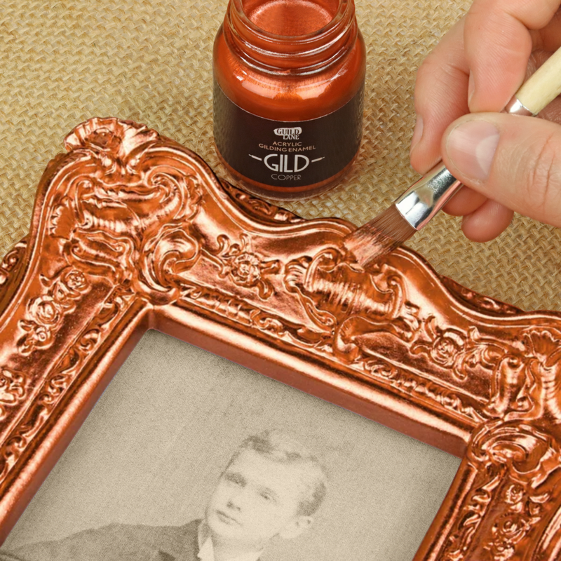 Person applying GILD gilding liquid to an ornate frame with a bottle of GILD gilding liquid nearby.