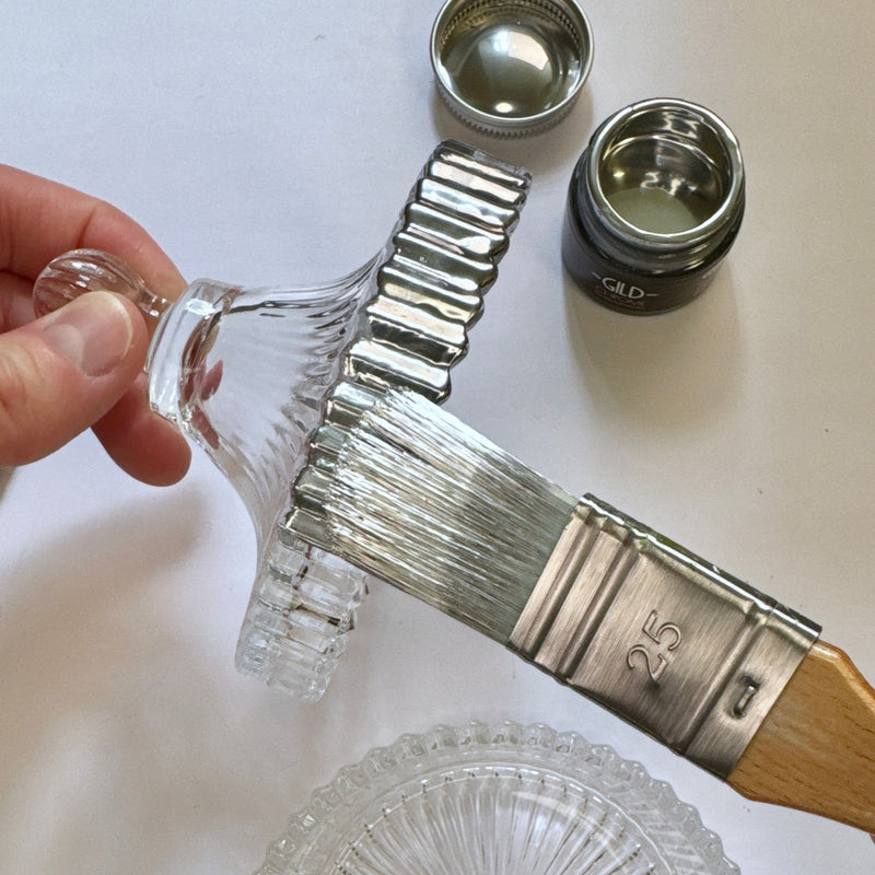Metallic chrome silver painting glass using brush with wooden handle and clear glass lid on a white background