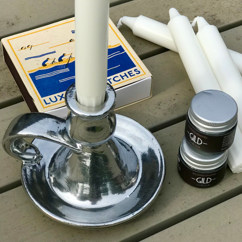 Chrome candle holder with a white candle, matches, and a small container on a wooden surface.