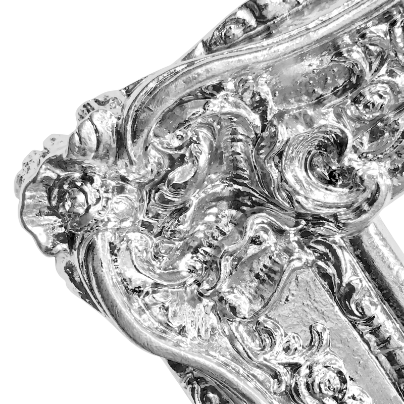 Close-up of an ornate silver frame with intricate chrome metallic paint on a white background