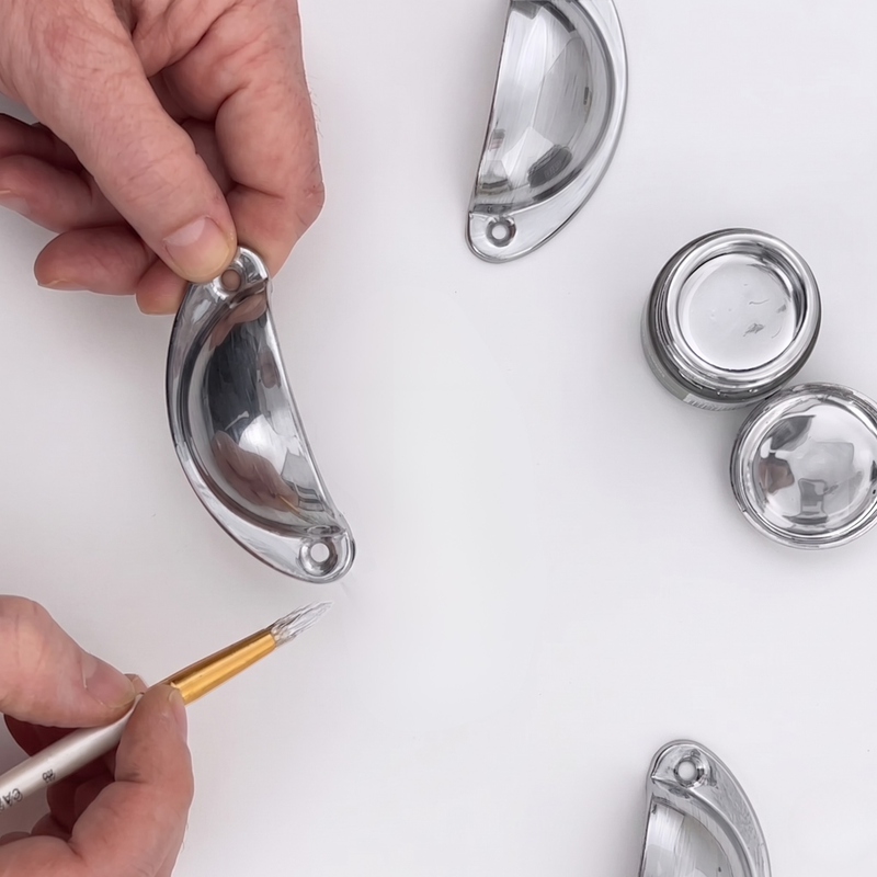 Metallic door handles being painted Chrome with a brush on a white background