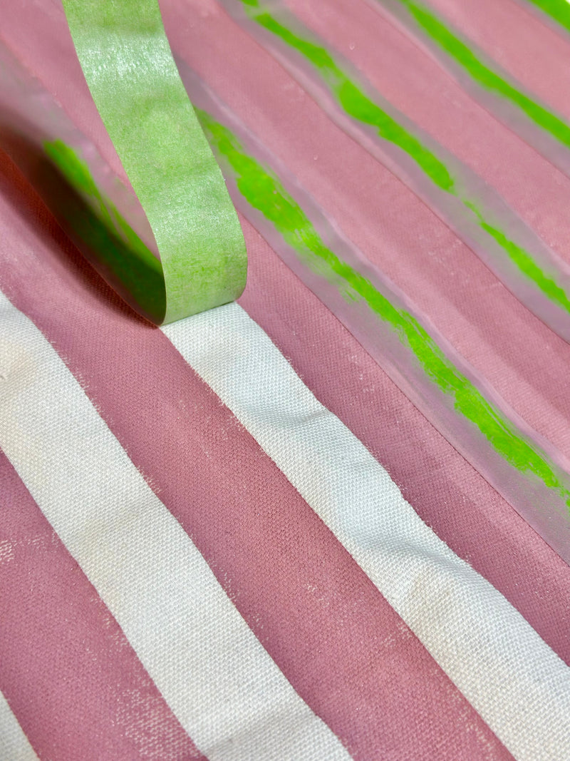 Close-up of pink and white striped fabric with green tape on a pink background