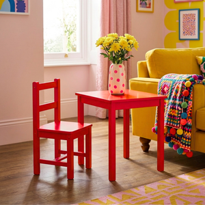 
                      
                        Table and chair painted in hot crimson pink red paint next to a bright yellow mustard sofa and a quirky multi coloured blanket
                      
                    