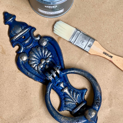 Decorative blue metal door knocker with a paintbrush and can of paint on a beige background