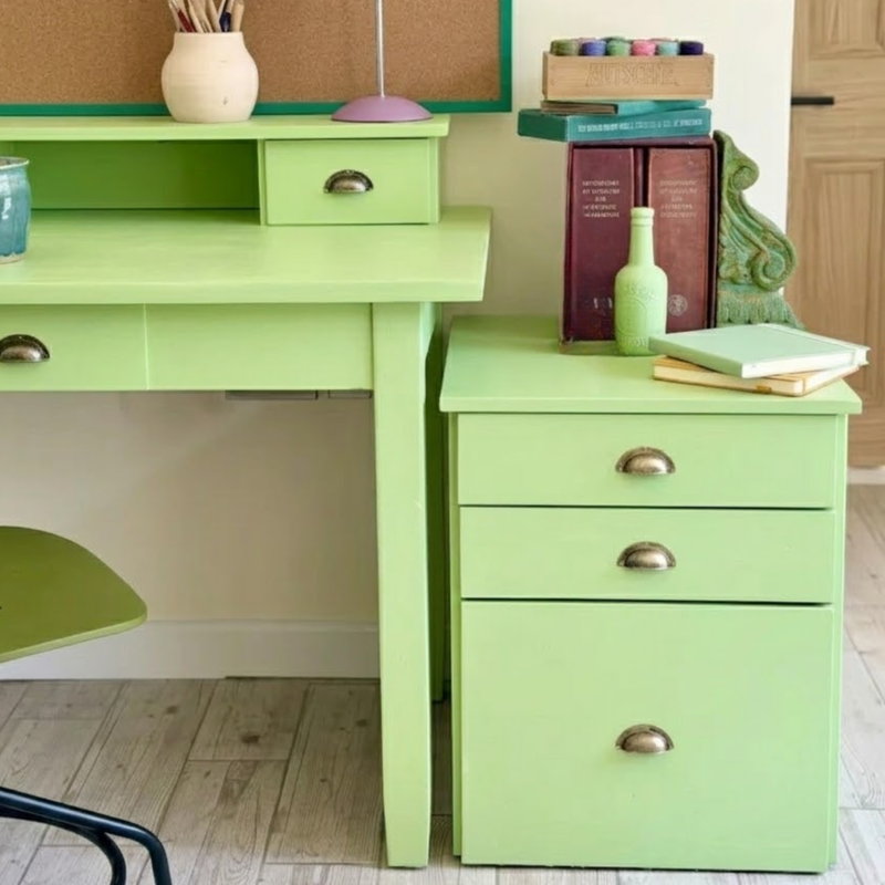 A bright lime green painted desk and matching three-drawer cabinet in a home office setting, styled with books, a lamp, and decorative items.