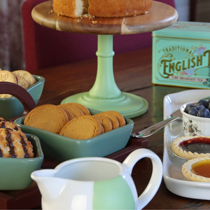 
                      
                        Painted green tea set with cookies, cakes, and tea bags on a wooden table.
                      
                    