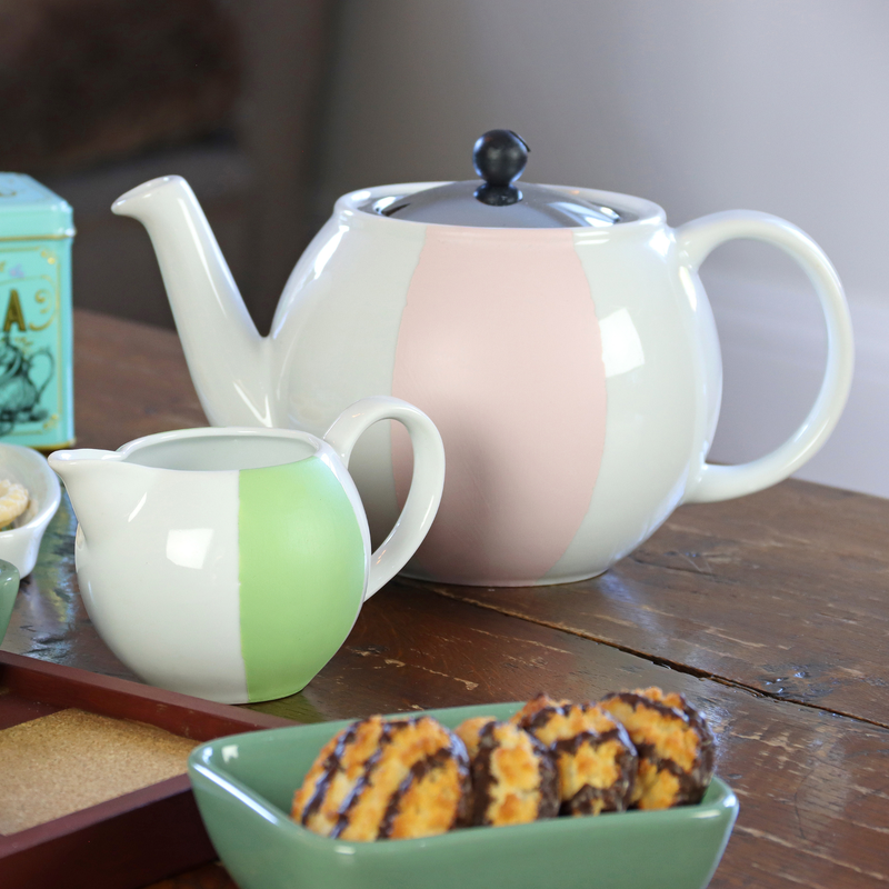 Two ceramic painted teapots on a wooden table with cookies and a tea canister.