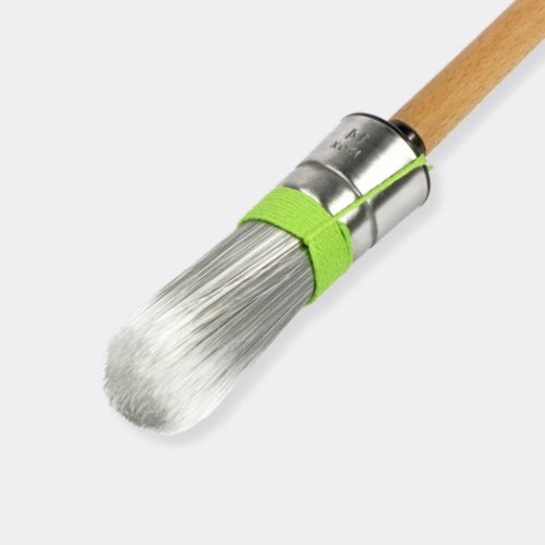 A close-up of a paintbrush with soft white bristles, a silver metal ferrule, a bright green band, and a light wood handle on a light gray background.