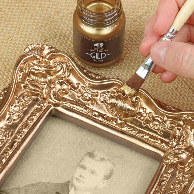Person applying bronze paint to an ornate picture frame using a brush.