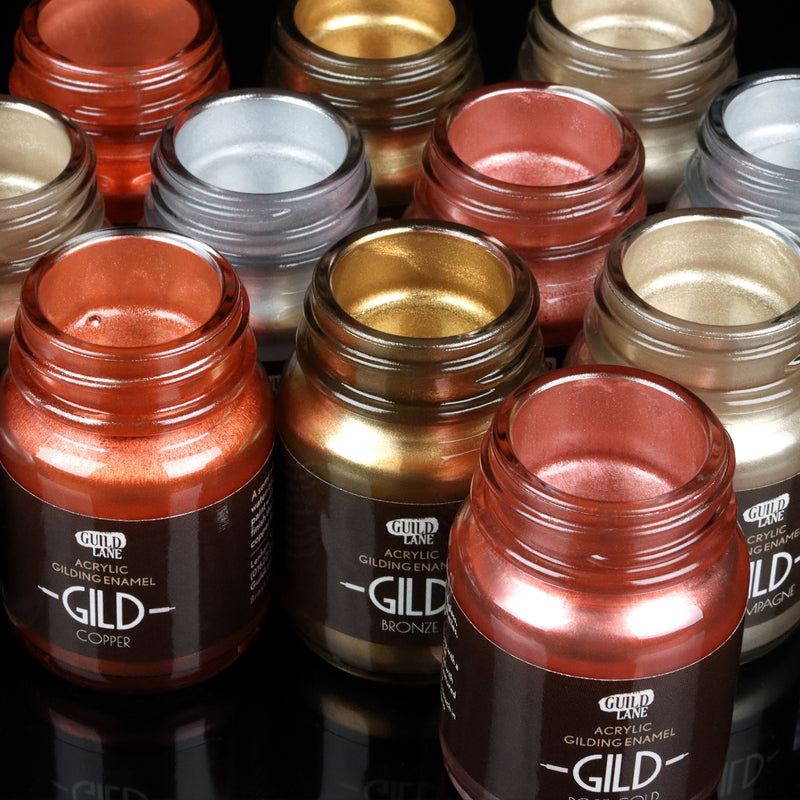 Collection of GILD acrylic gilding enamel jars in various metallic colors on a reflective surface.