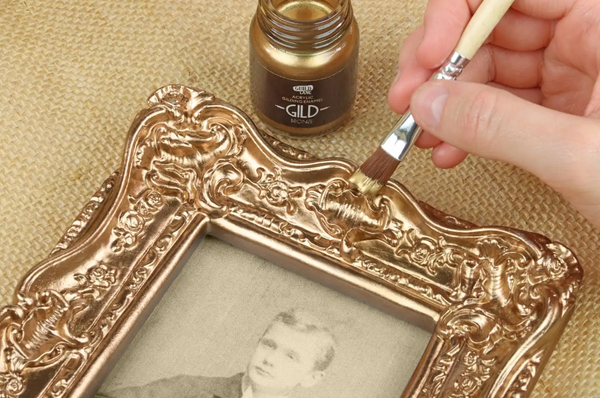 Person applying gold paint to an ornate picture frame using a brush.