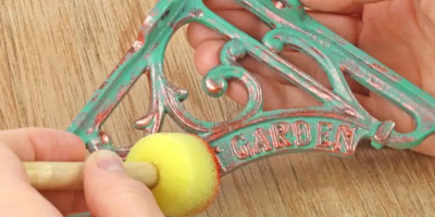 Person painting a decorative bracket with a yellow sponge on a wooden surface