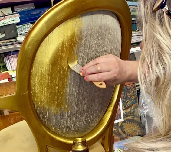 Person painting a gold circle on a wooden frame with a brush.