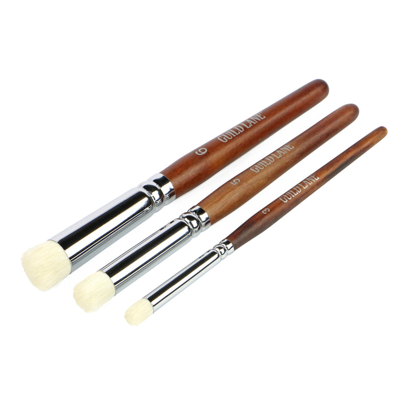 Three dry brush brushes with wooden handles and white bristles on a white background