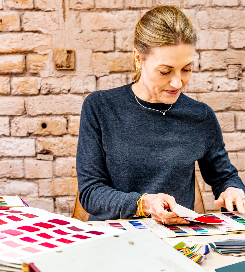 Founder Jeni working with paint colour swatches against a brick wall.