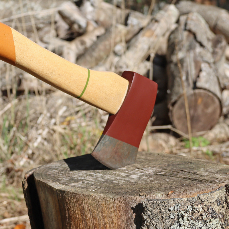 Wooden-handled axe on a log with blurred logs in the background, painted metal blade.