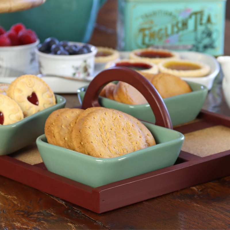 Tea party setting with cookies, tea, and fruit on a wooden table, all in a painted tray.