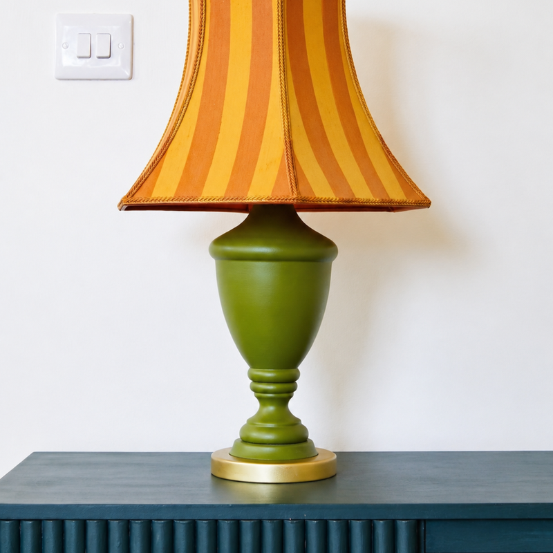 Green lamp with a striped orange and yellow shade on a dark surface.