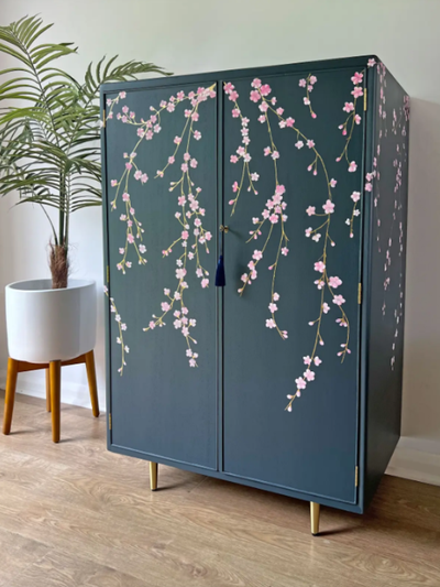 Blue cabinet with floral design in a room with a plant and wooden floor.