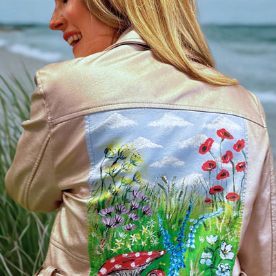 Woman wearing a beige jacket with a painted floral design painted on the back.
