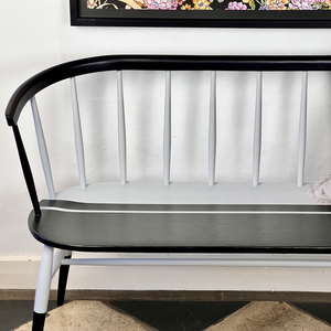 
                      
                        White bench with black armrests and seat against a white wall.
                      
                    