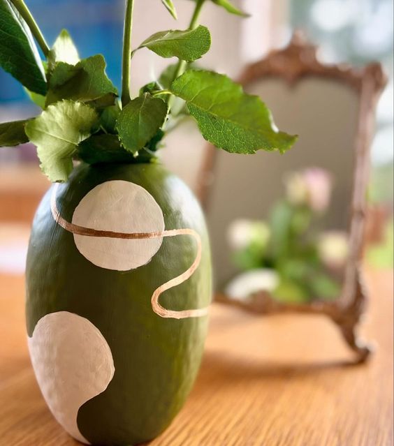 Decorative green vase with white circular patterns on a wooden surface