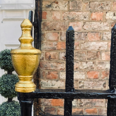 Decorative black metal railing with a gold finial against a brick wall.