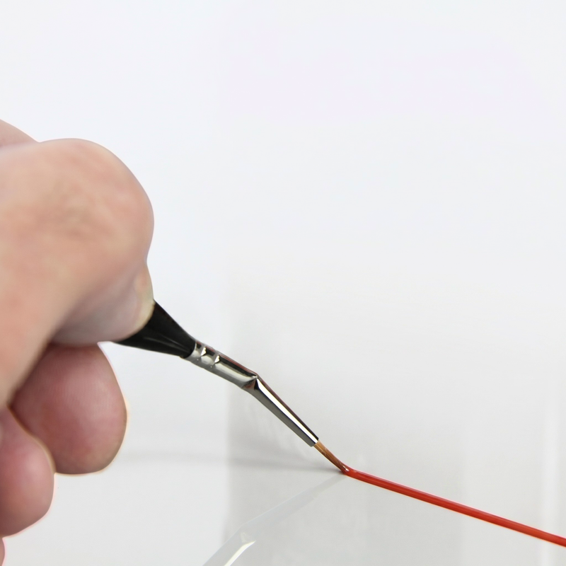 Hand holding a paintbrush with red paint on a white background